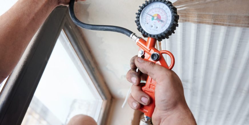 Close up plumber filling pipes with pressurized air to inspect for leaks in new heating system installation. Worker using manometer or pressure gauge, checking gas tightness of heating system.